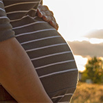 A pregnant woman standing outside in a nature setting.