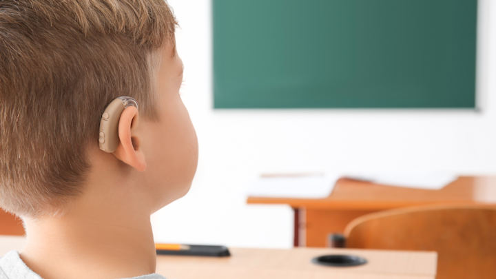 A young child sitting in class wearing a hearing aid.